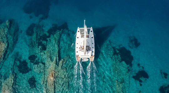 Vue aérienne d'un catamaran blanc naviguant sur les eaux turquoise de la mer Égée en Grèce
