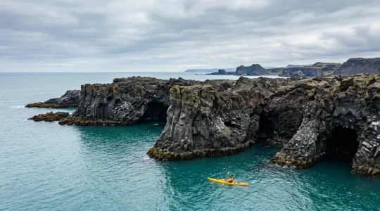 Kayakiste naviguant le long de formations géologiques spectaculaires d'une côte volcanique inaccessible par voie terrestre