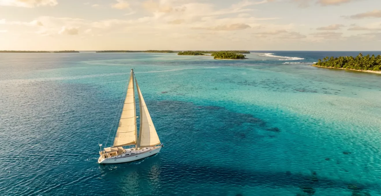 Voilier naviguant entre les atolls du Pacifique Sud avec lagon turquoise et ciel immaculé
