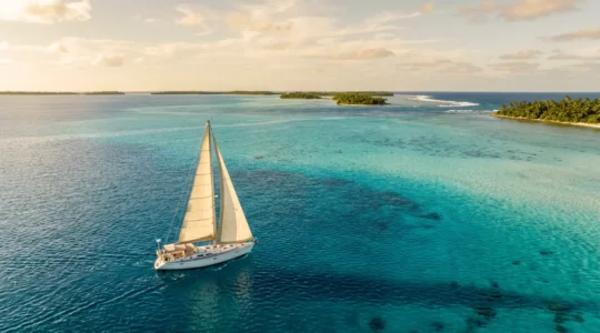 Voilier naviguant entre les atolls du Pacifique Sud avec lagon turquoise et ciel immaculé